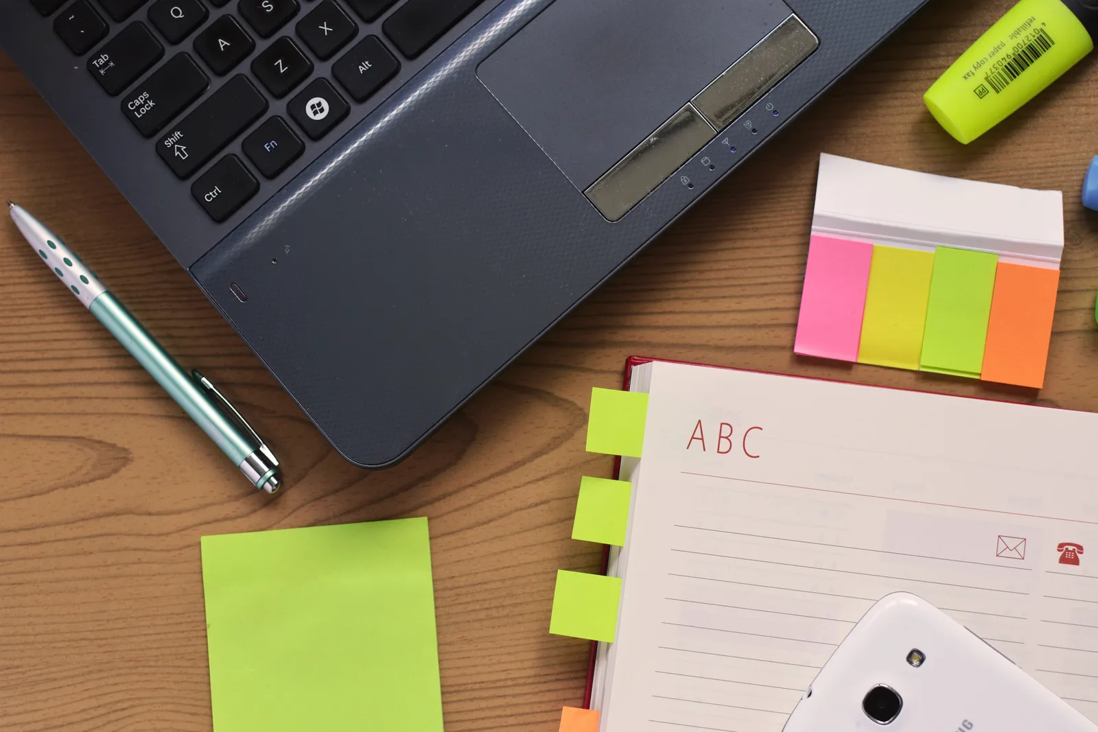 Laptop, notebook and pen laid out on a work desk