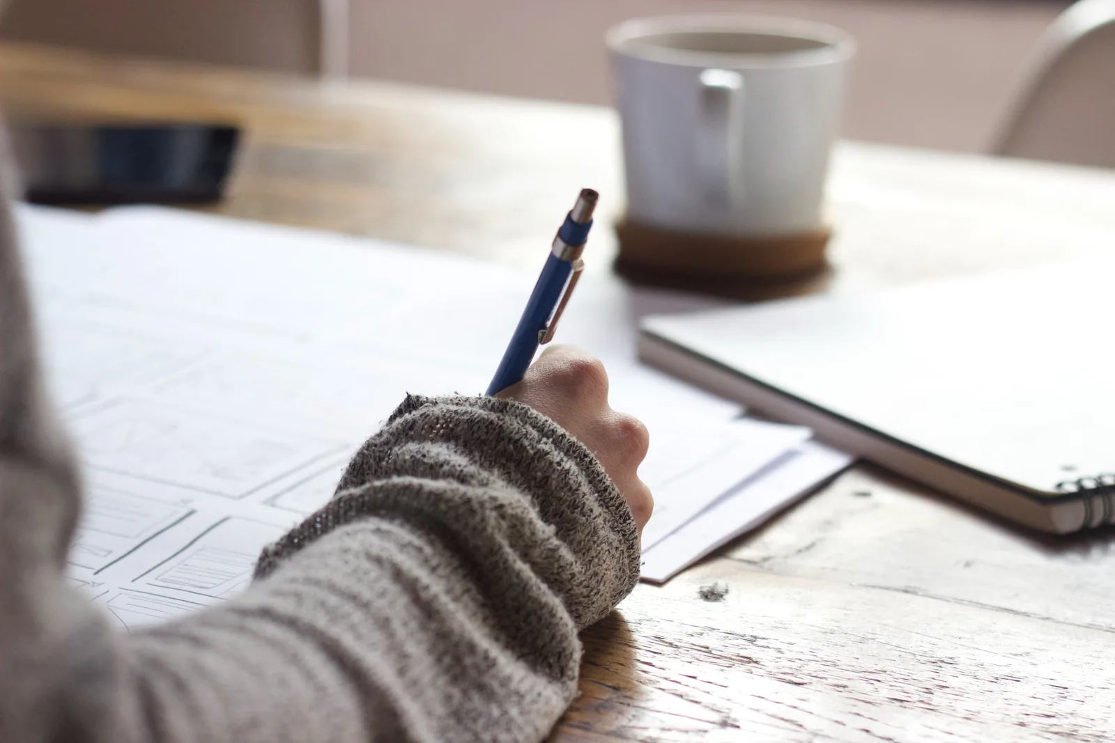Person sketching a website plan in a notebook next to a coffee mug